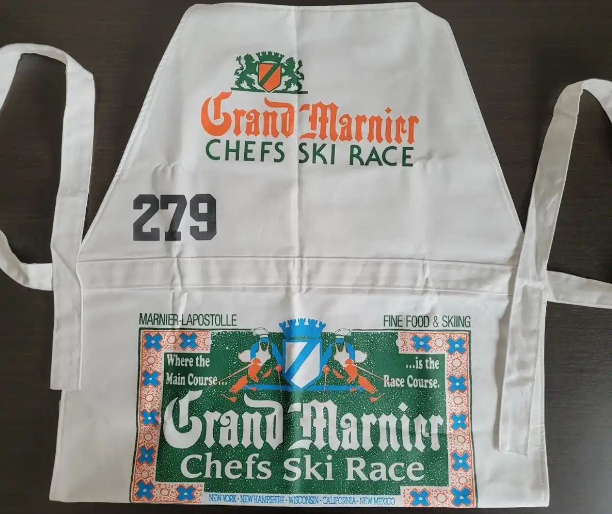 A white apron with 'Grand Marnier Chefs Ski Race' branding, featuring a race number 279 and a graphic with skiers and the…
