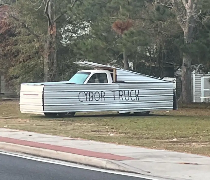 A pickup truck is heavily modified with corrugated metal siding, resembling a futuristic or industrial design, parked on a…