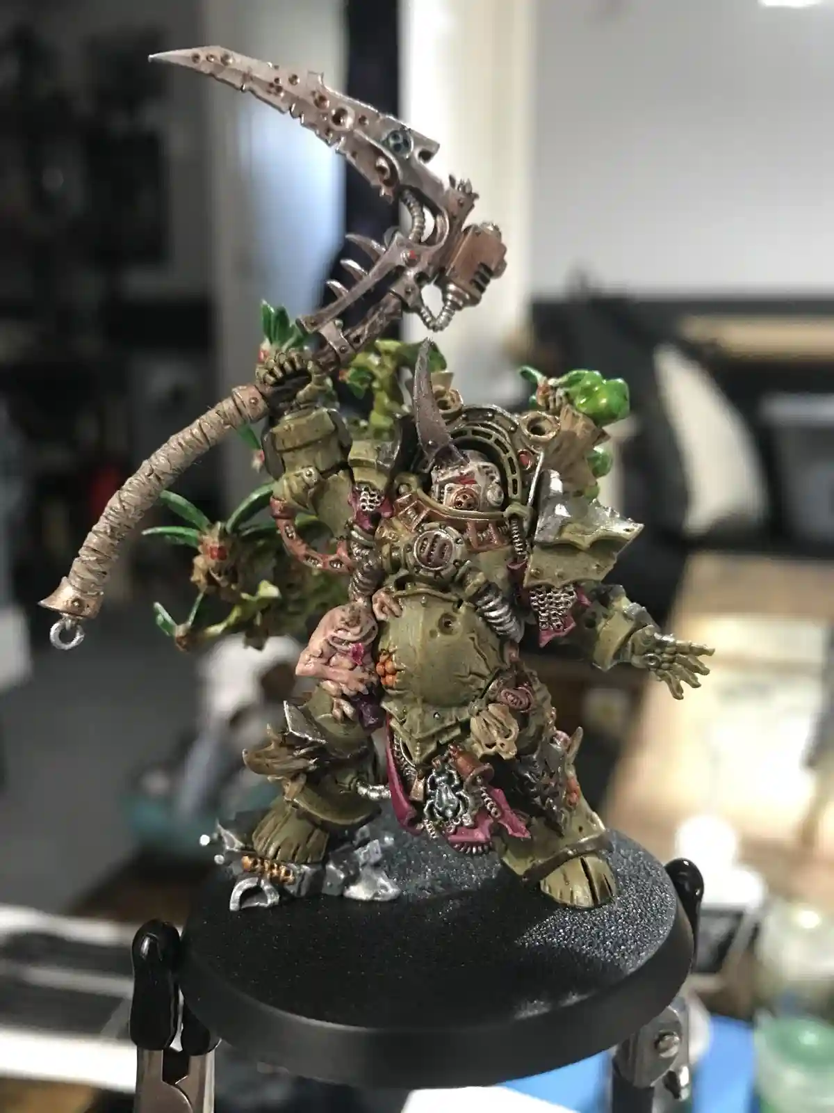 A heavily detailed, green-painted miniature of a grotesque, biomechanical warrior with a large, ornate scythe-like weapon…