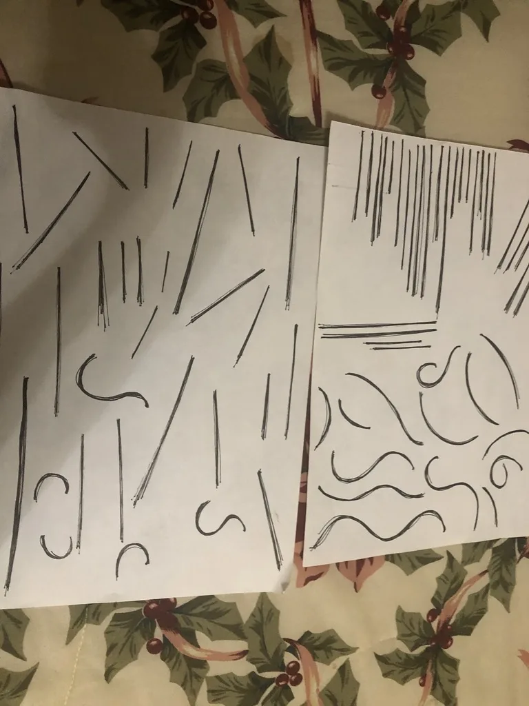 Two sheets of paper with messy, abstract scribbles and lines drawn in black ink lie on a holly-patterned fabric. The left…
