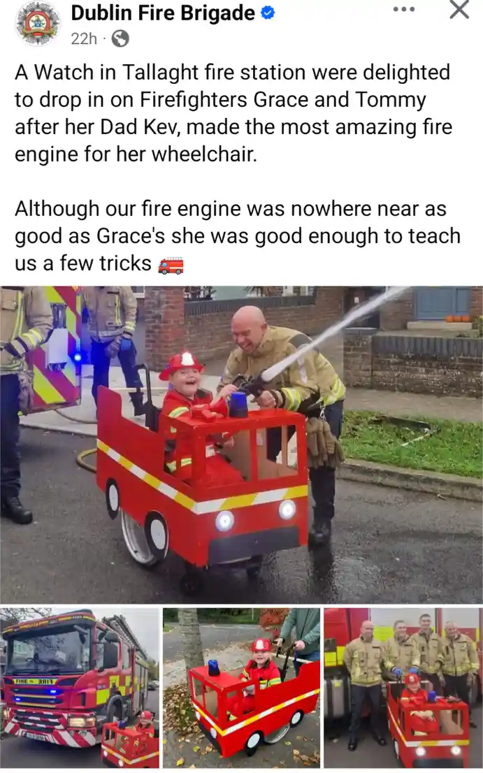 A young girl in a red firefighter costume sits happily in a custom-built red wheelchair shaped like a fire engine, while a…