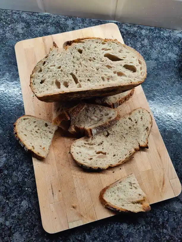 A rustic, artisanal loaf of bread with a golden-brown crust and airy crumb is sliced and arranged on a wooden cutting board…