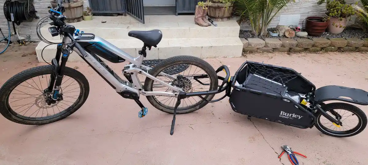A silver and black electric mountain bike with a 'BULLS' frame and 'BOSCH' motor is parked on a concrete patio, attached to…