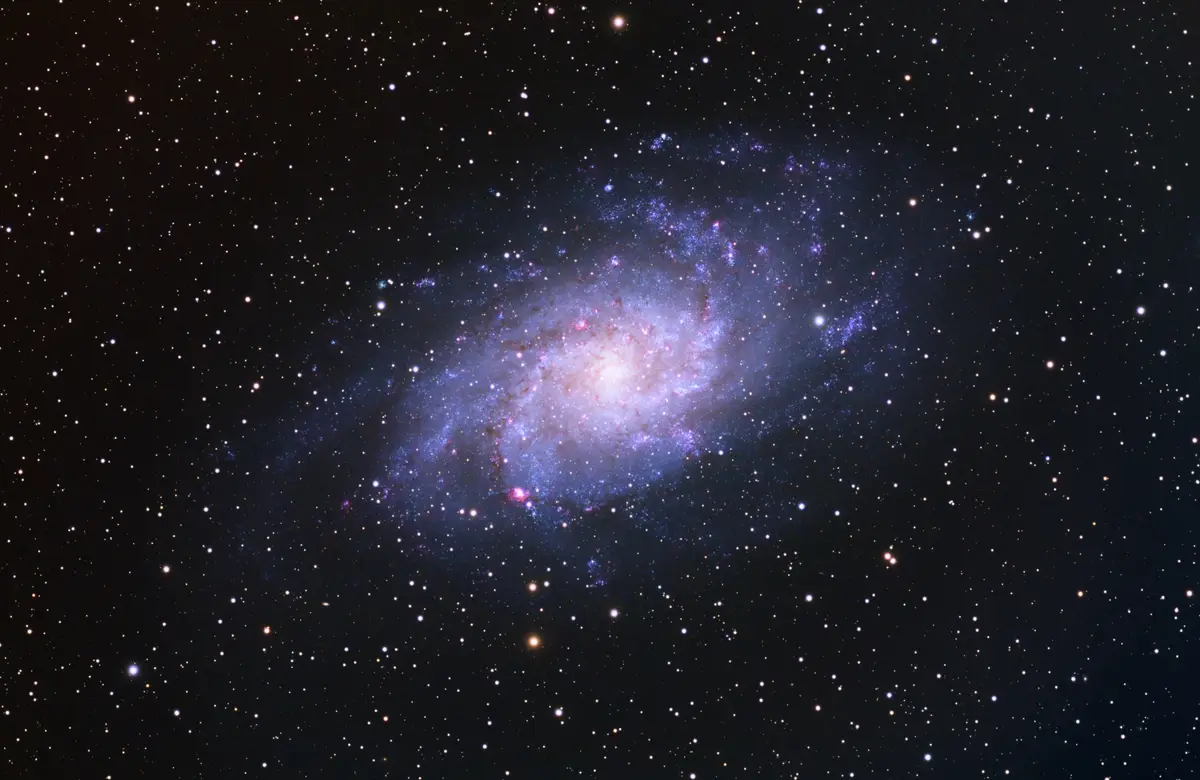 A stunning astronomical photograph shows a spiral galaxy with a bright central core and swirling arms of blue and pink…