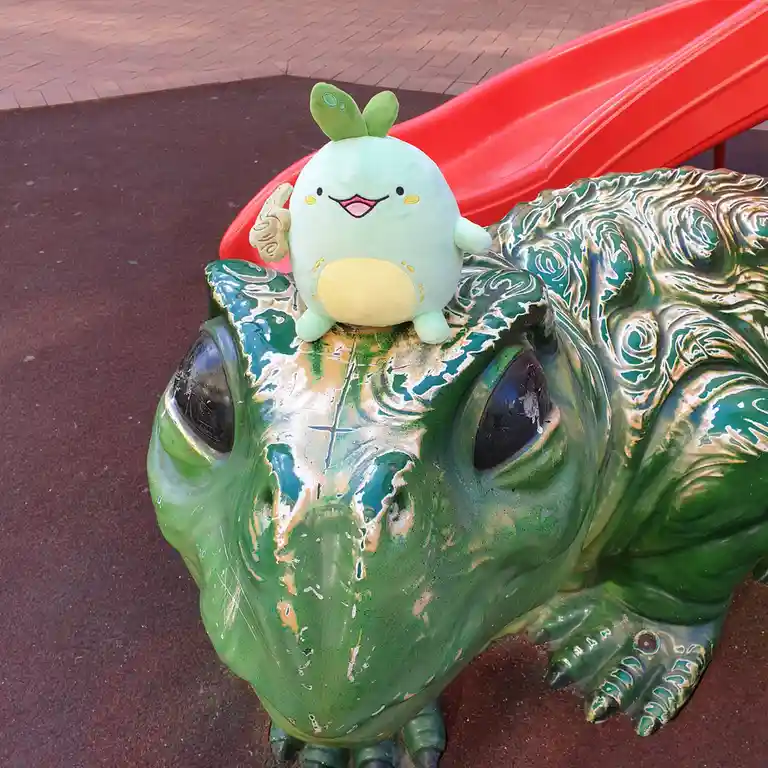 A light green, round, smiling plush toy with leaf-like ears and a yellow belly sits atop the head of a large, weathered…
