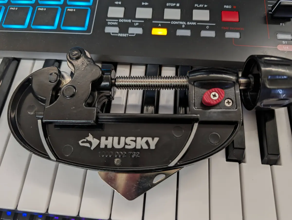 A black Husky brand pipe wrench is clamped onto the white and black keys of a keyboard, with the instrument's control panel…