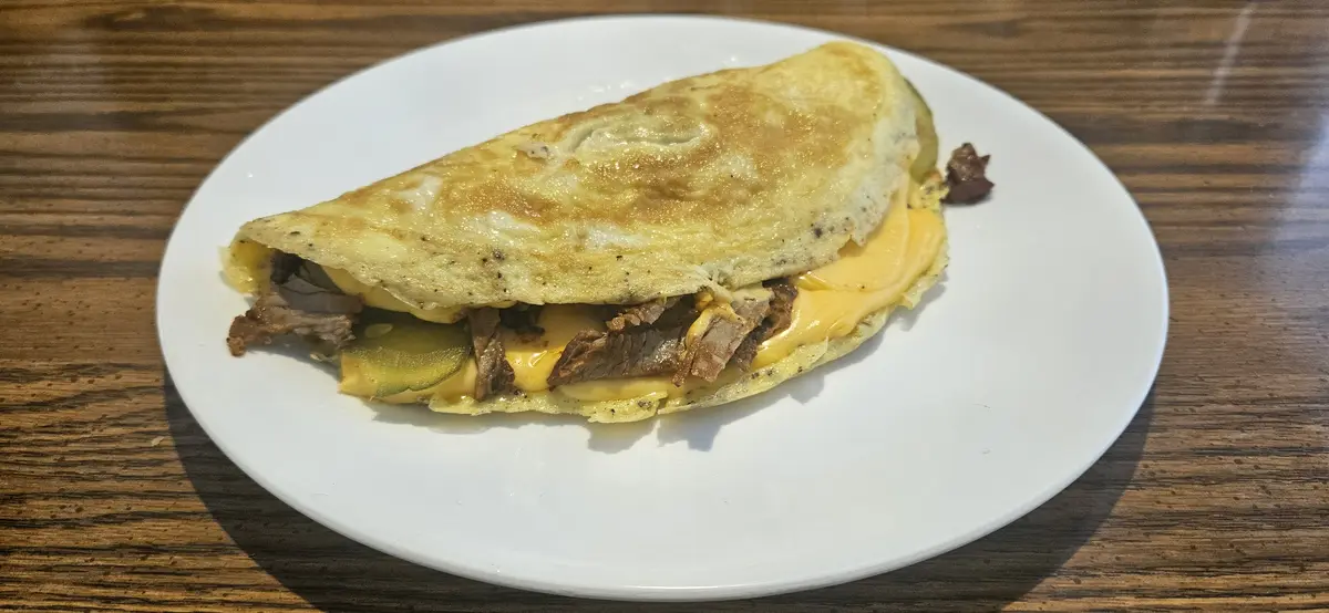 A close-up photo shows a folded, golden-brown omelette on a white plate, revealing melted yellow cheese, shredded meat, and…