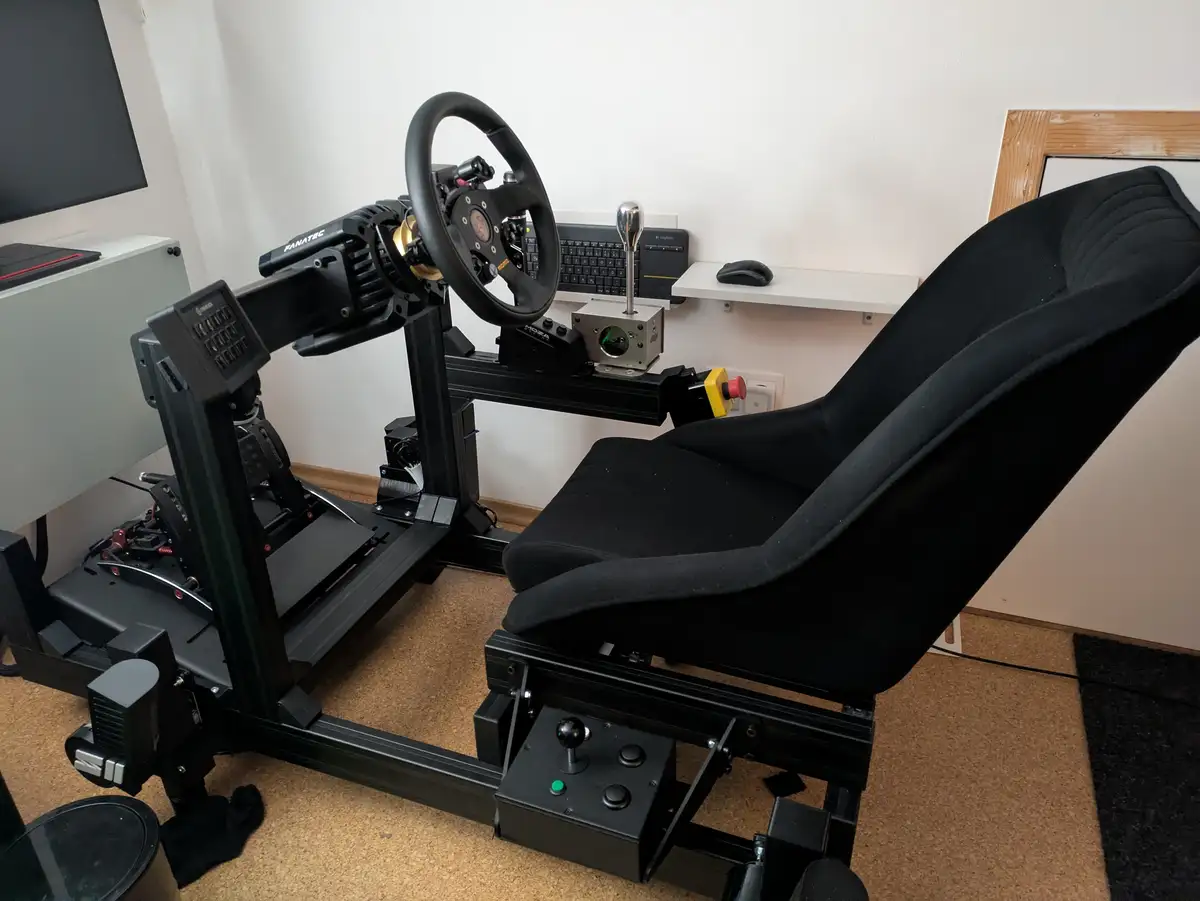 A high-end racing simulator setup featuring a black racing seat, a Panatec steering wheel, a gear shifter, and pedals, all…