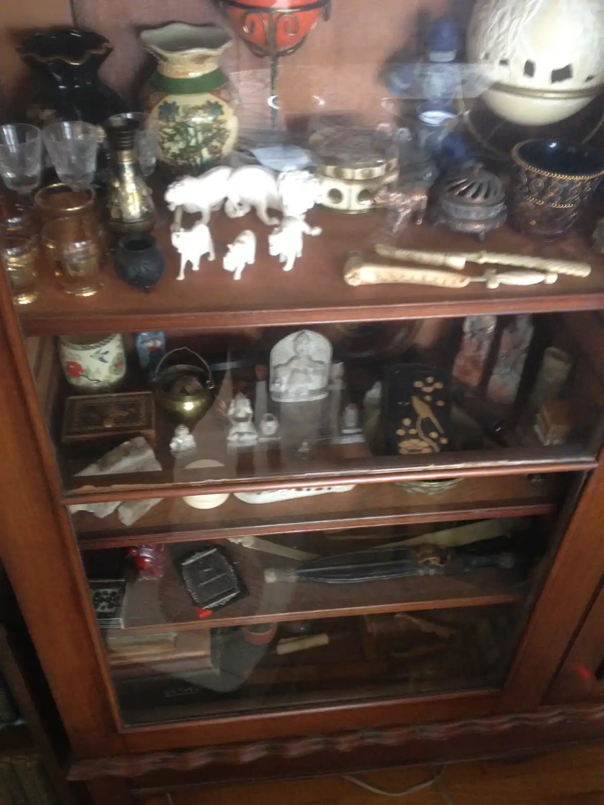 A wooden display cabinet filled with various eclectic and mismatched items including vases, figurines, glassware, and…