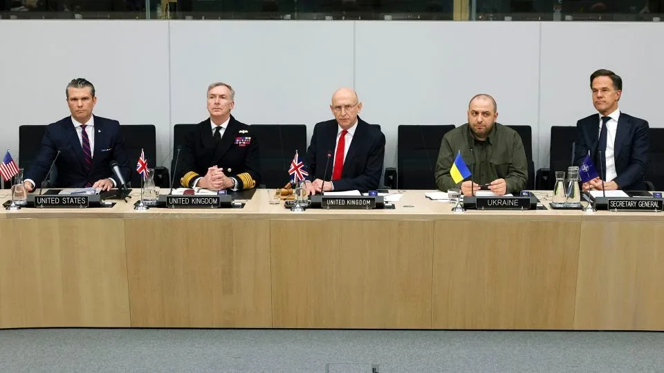five men sit at a long conference table with nameplates reading 'UNITED STATES', 'UNITED KINGDOM', 'UKRAINE', and 'SECRETARY…