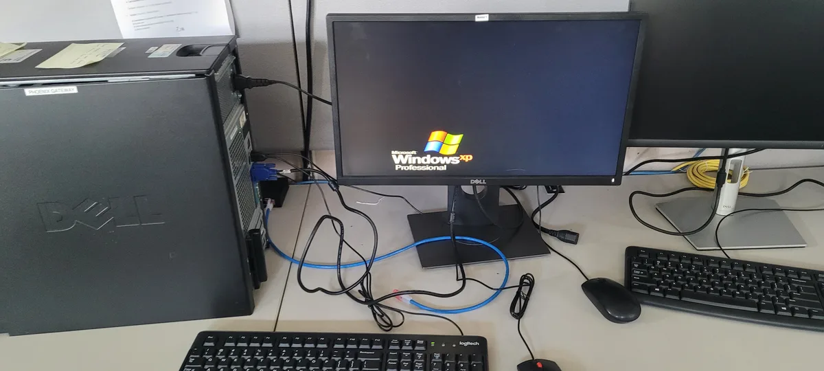 A Dell desktop computer with a monitor displaying the Windows XP Professional startup logo, surrounded by tangled cables and…
