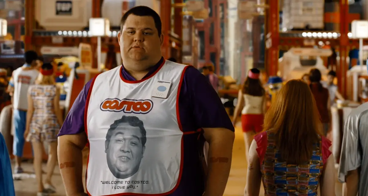 A man in a Costco vest with a photo of himself and the text 'WELCOME TO COSTCO. I LOVE YOU.' on it, standing in a crowded…