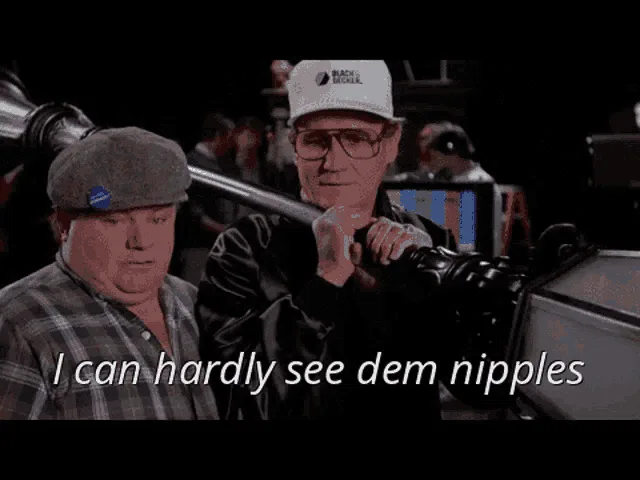 Two men are in a film set environment, one wearing a grey flat cap and plaid shirt, the other wearing a white 'Black McCall'…