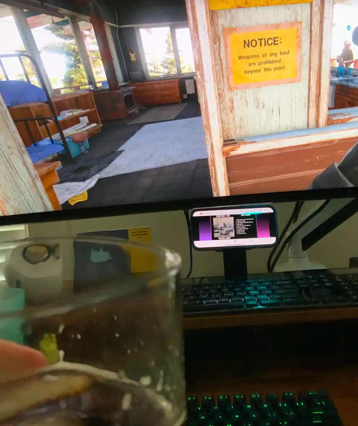 A photo shows a computer monitor displaying a video game scene with a yellow notice sign that reads 'NOTICE: Weapons of any…
