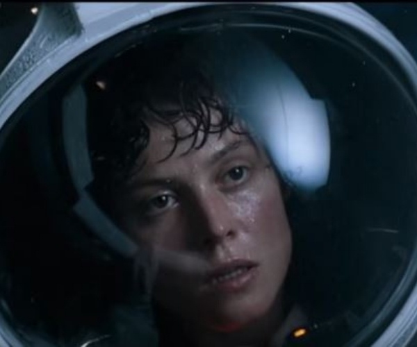 A close-up shot of a woman in an astronaut helmet, her face wet and expression tense, looking directly at the viewer. The…
