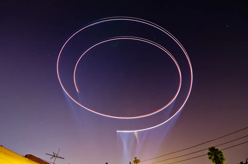 A long-exposure night sky photo shows two glowing, concentric circular light trails against a starry purple sky, with faint…