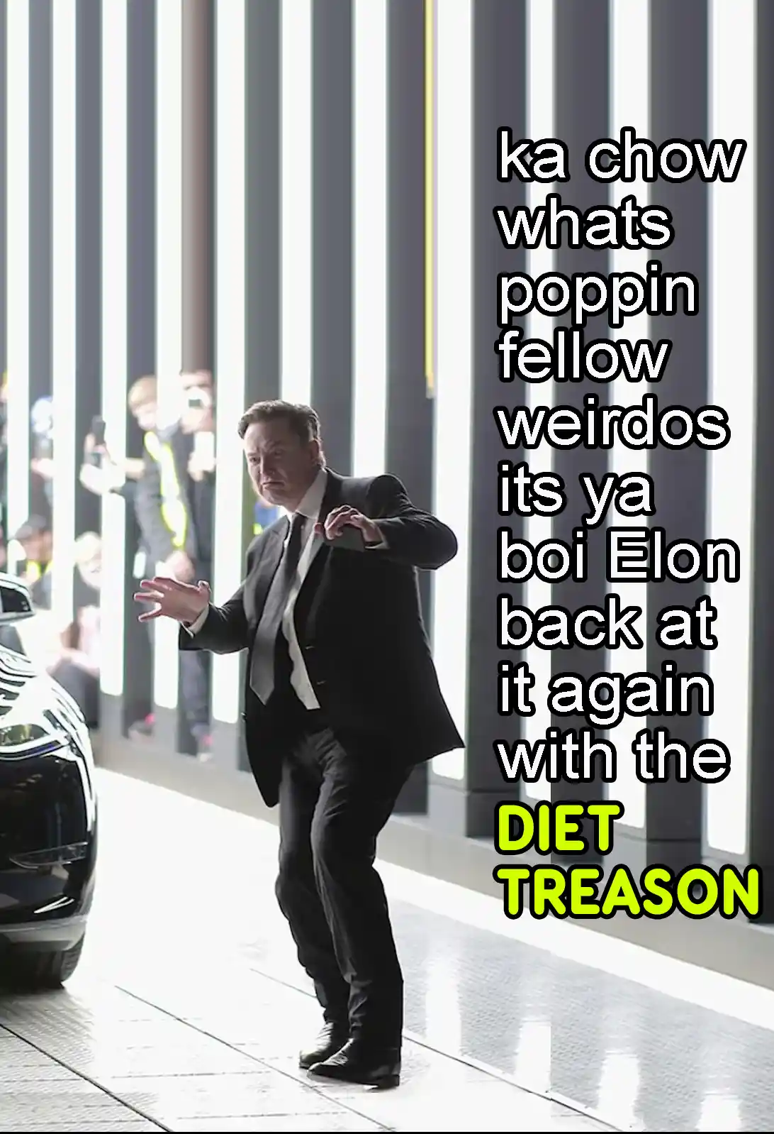 A man in a black suit and tie is captured mid-stride, gesturing with both hands, standing next to a sleek black car. Behind…
