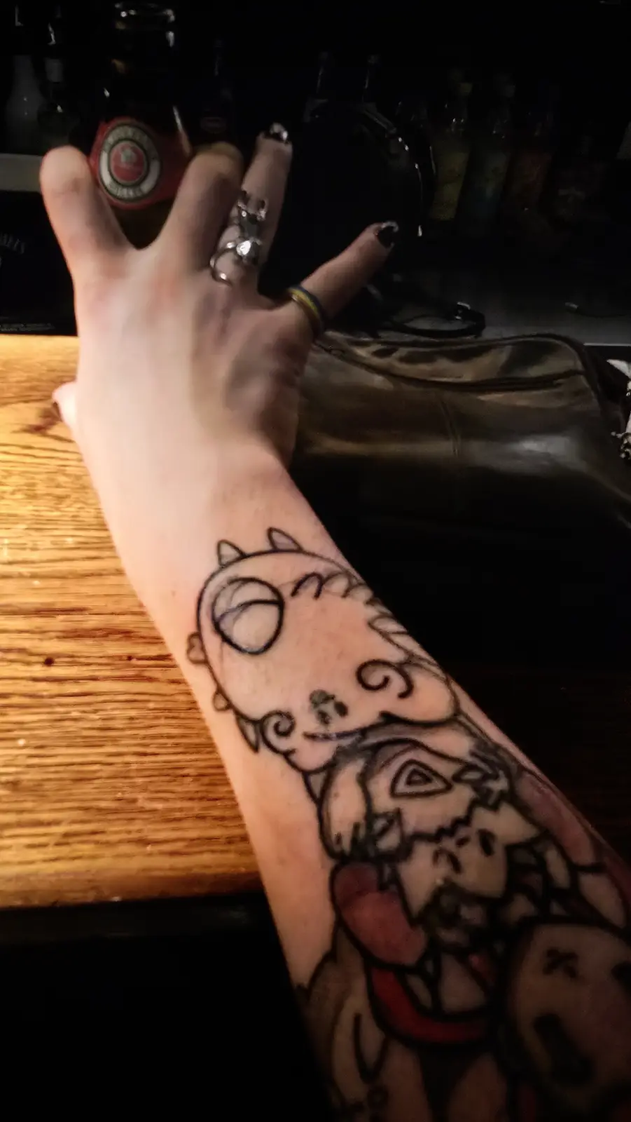 A person's forearm is shown with a black-and-gray tattoo of a cartoon cat and a dog, with the person's hand resting on a…