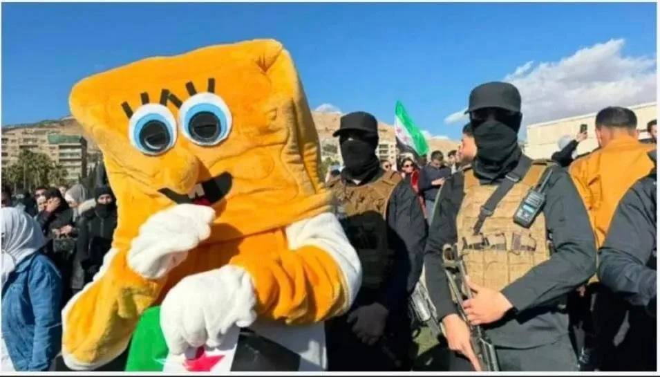 A person in a large, yellow SpongeBob SquarePants mascot costume stands in front of armed men in tactical gear and black…
