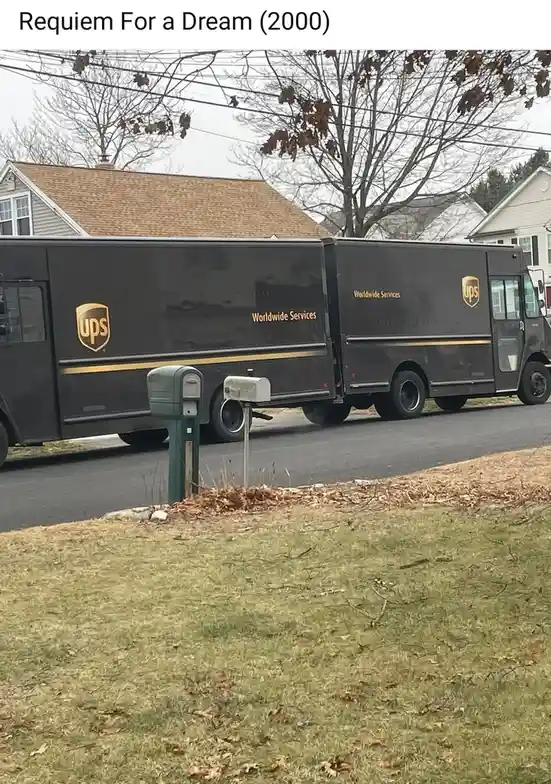 A black UPS delivery truck is parked on a residential street next to a green and a white mailbox. The image has text at the…