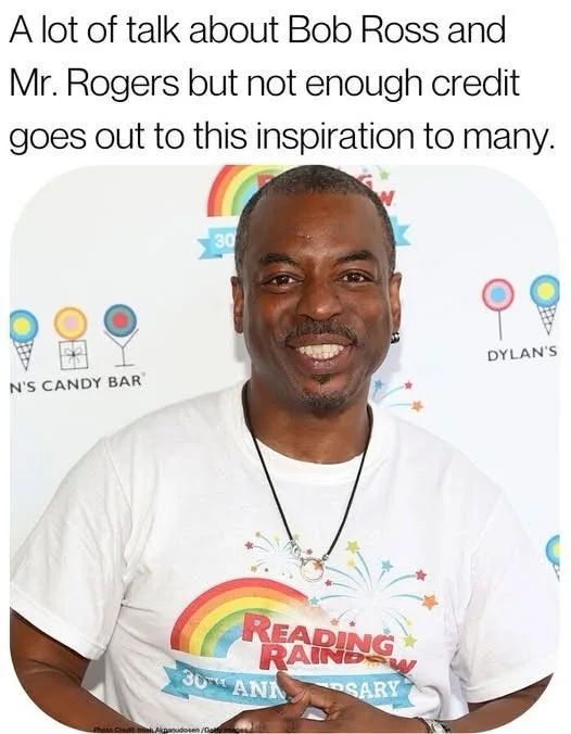 A smiling Black man with a goatee and earring wears a white t-shirt with a rainbow, fireworks, and text reading 'READING…