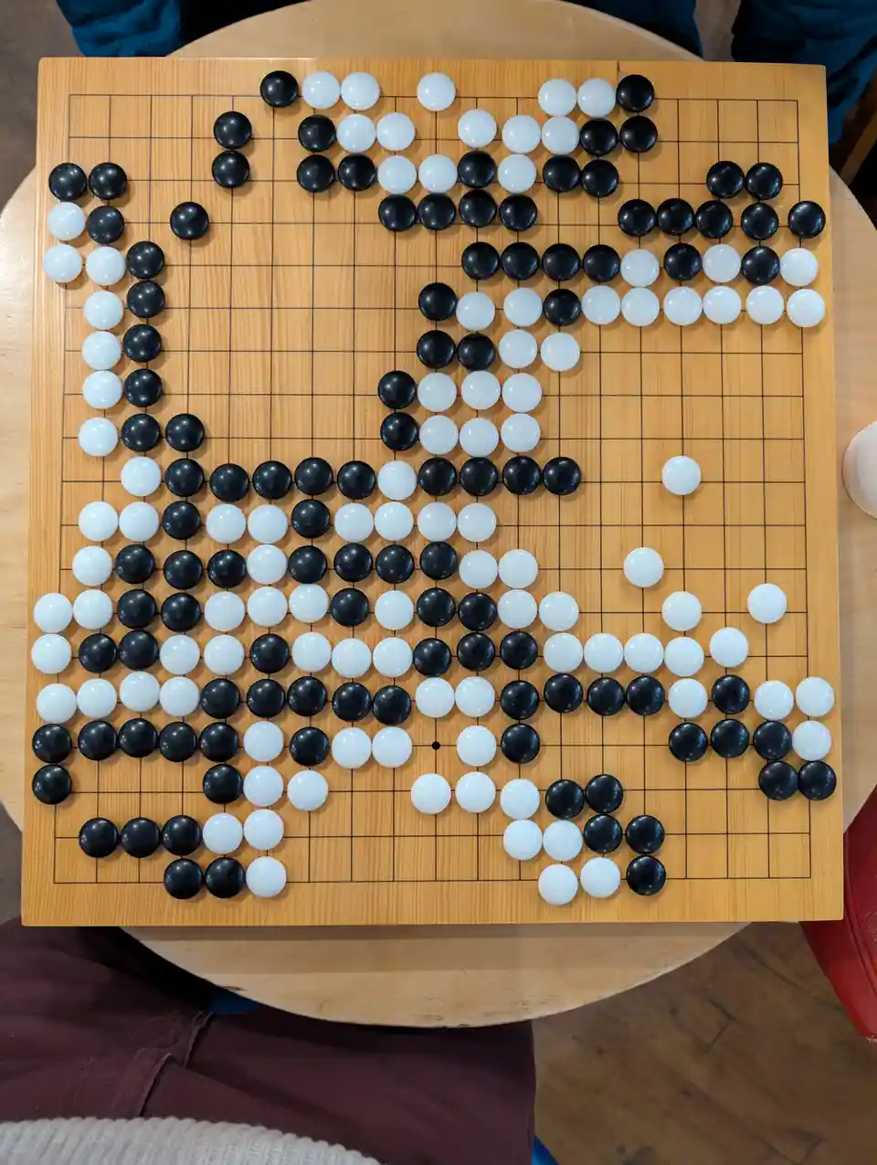 A top-down photo of a Go board with black and white stones arranged to form the silhouette of a person's face, with the…