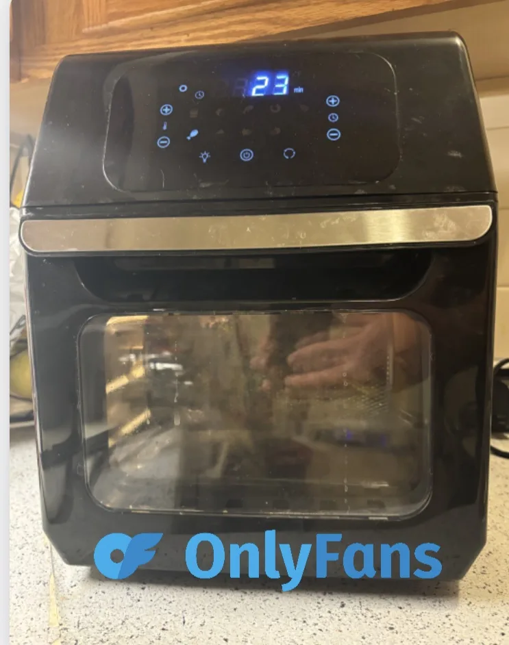 A black countertop toaster oven with a digital display showing '23 min' is pictured on a speckled kitchen counter. The…