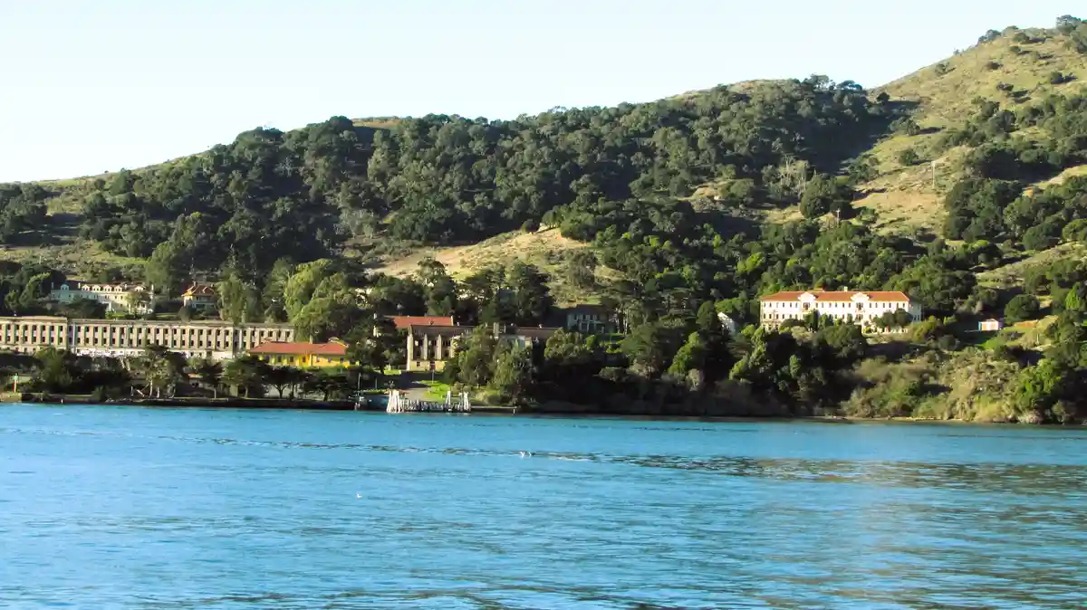 a scenic view of alcatraz island with its historic buildings nestled among green hills overlooking a large body of blue…