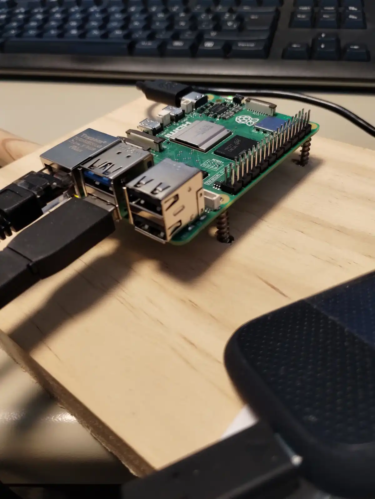 A green raspberry pi single-board computer is mounted on a wooden board with screws, surrounded by various cables and ports…