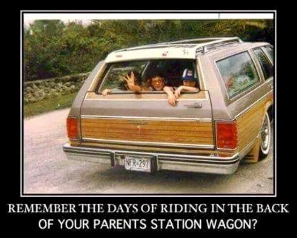 The image shows the rear view of a vintage wood-paneled station wagon with two children leaning out the back window, waving…