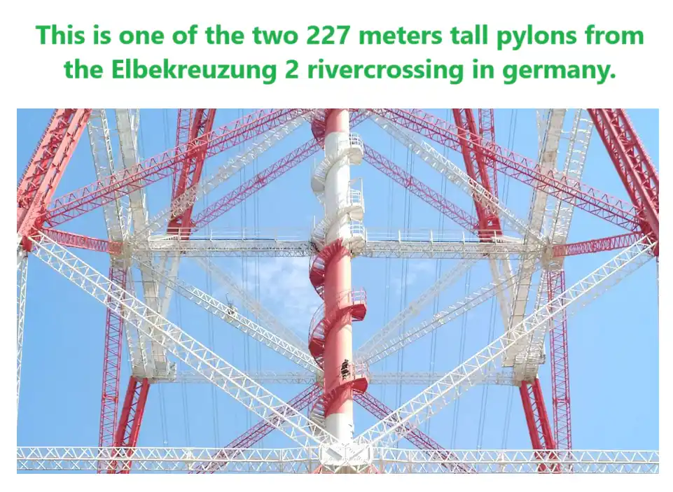 The image shows a massive red and white lattice pylon structure against a clear blue sky, with a spiral staircase winding up…