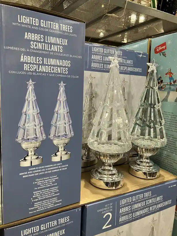 A retail display of clear, faceted, glitter-filled Christmas trees with silver bases, shown next to their product boxes…