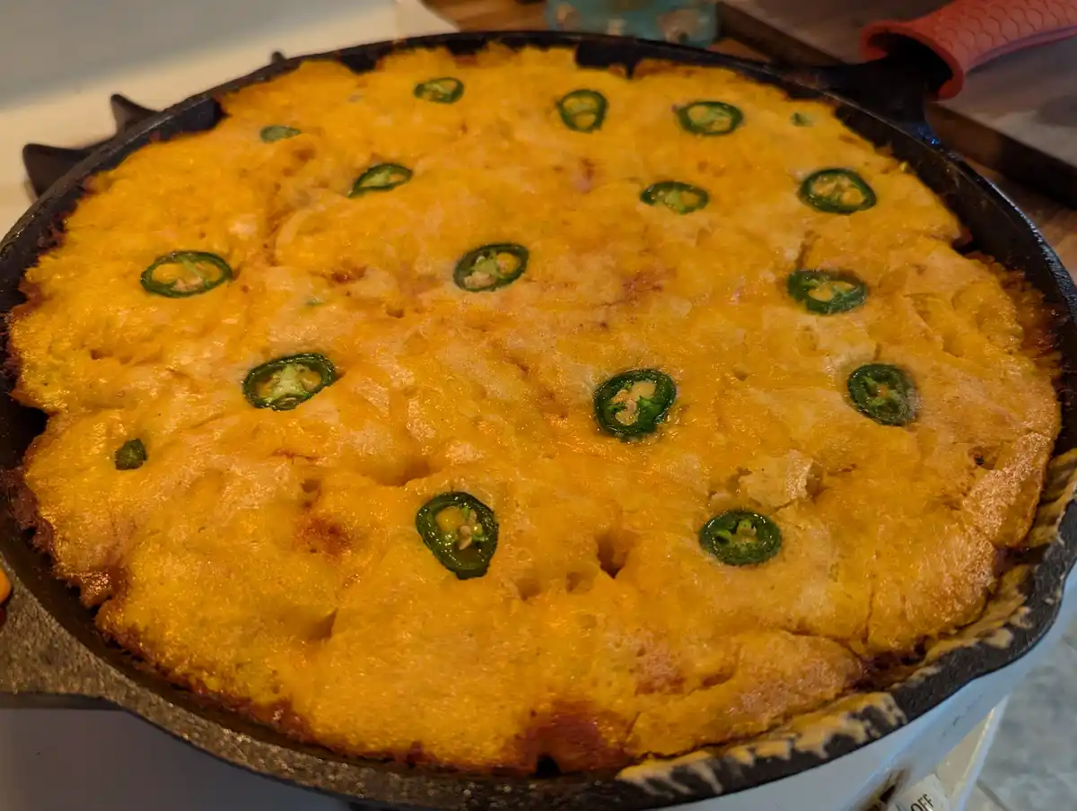 a close-up photo of a golden-brown baked dish in a black cast-iron skillet, topped with melted cheese and scattered green…