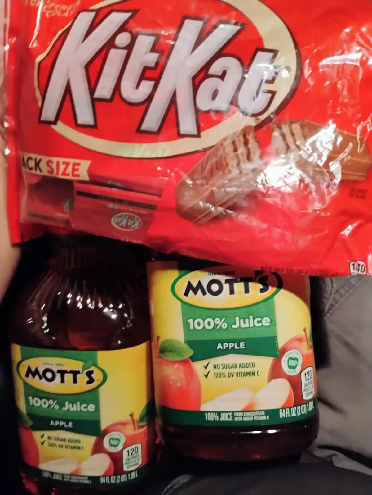A red bag of KitKat chocolate bars is held above two bottles of Mott's 100% Apple Juice, creating a visual pun. The overlaid…