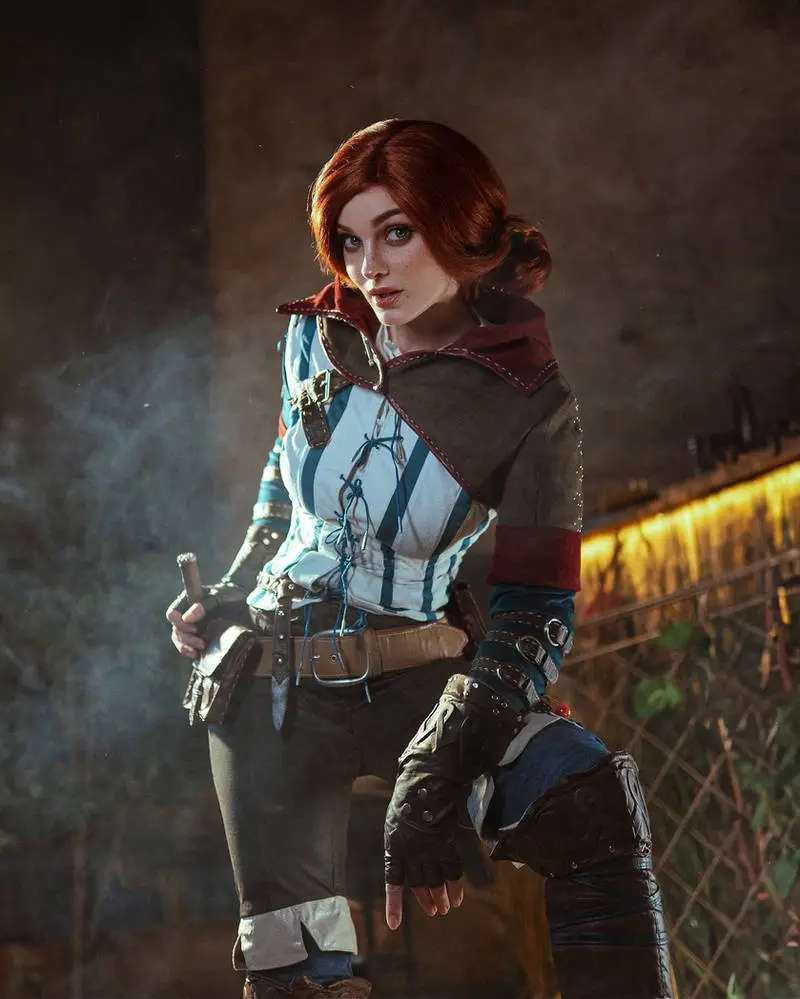 A person in a detailed cosplay of the video game character Ciri from The Witcher, standing in a dimly lit, smoky environment…