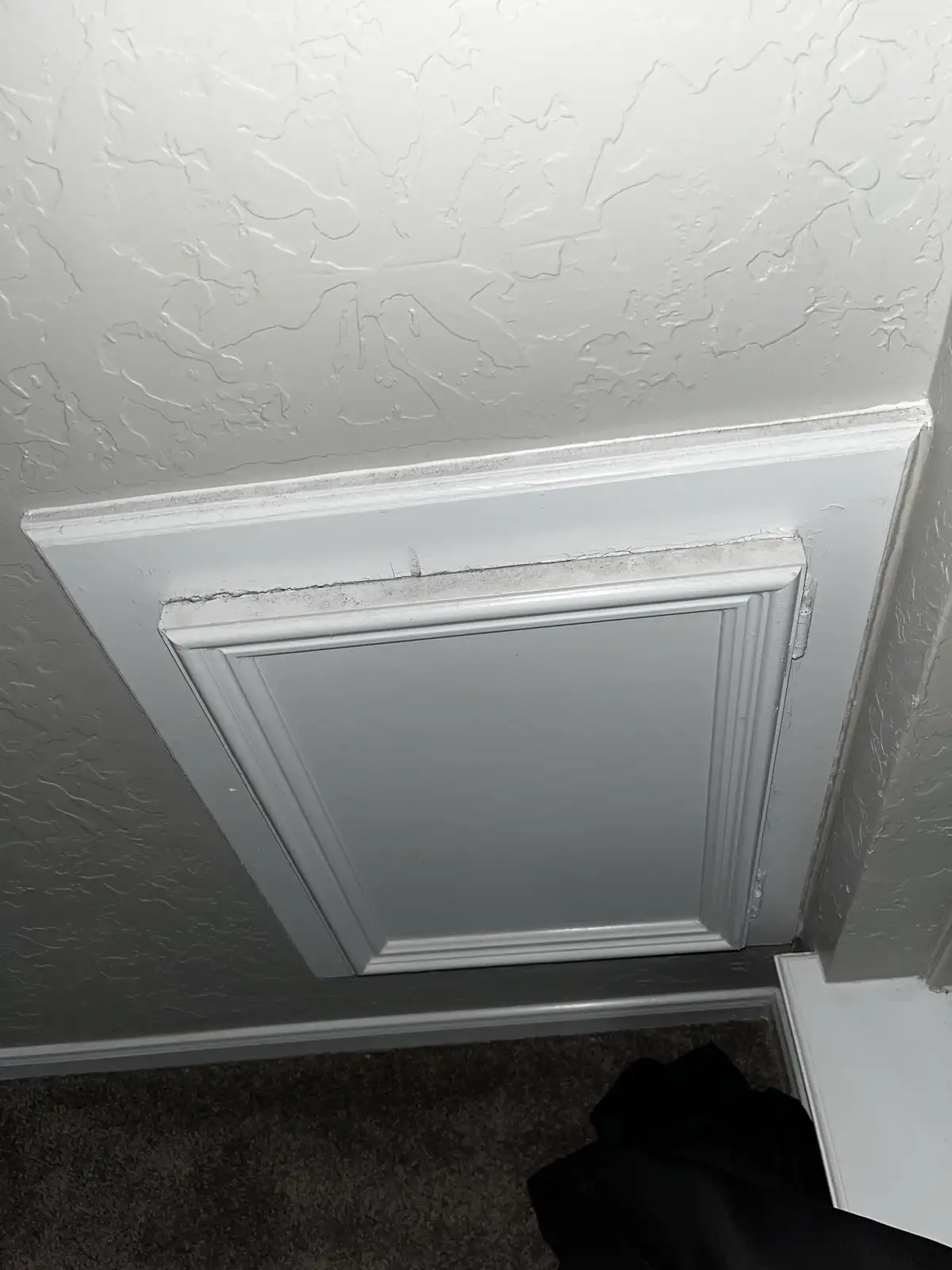 A close-up photo shows a white textured wall meeting a white wainscoting panel, with visible cracks and peeling paint along…