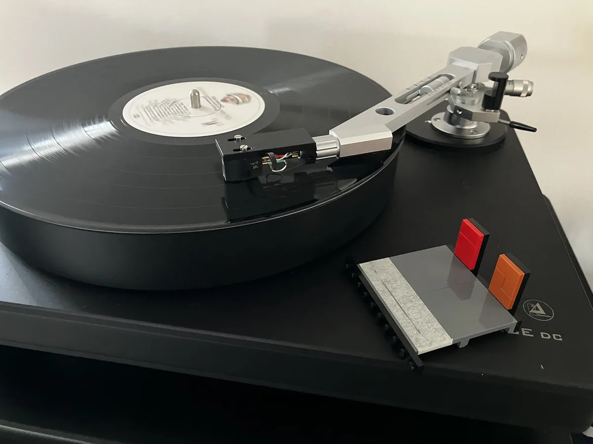 A close-up photo of a high-end turntable with a vinyl record spinning, featuring a silver tonearm and a small Lego structure…