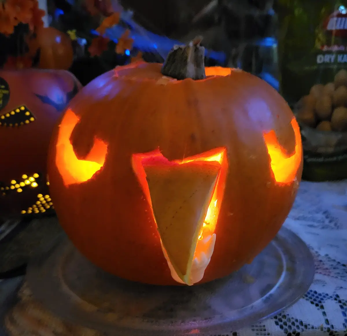 A close-up of a carved Halloween pumpkin with glowing orange eyes and a triangular mouth, which is filled with a wedge of…