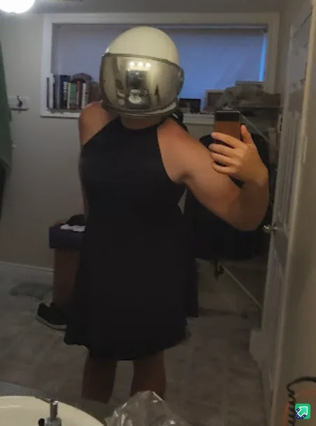 A person wearing a full-face motorcycle helmet with a reflective visor stands in a bathroom mirror, taking a selfie with a…