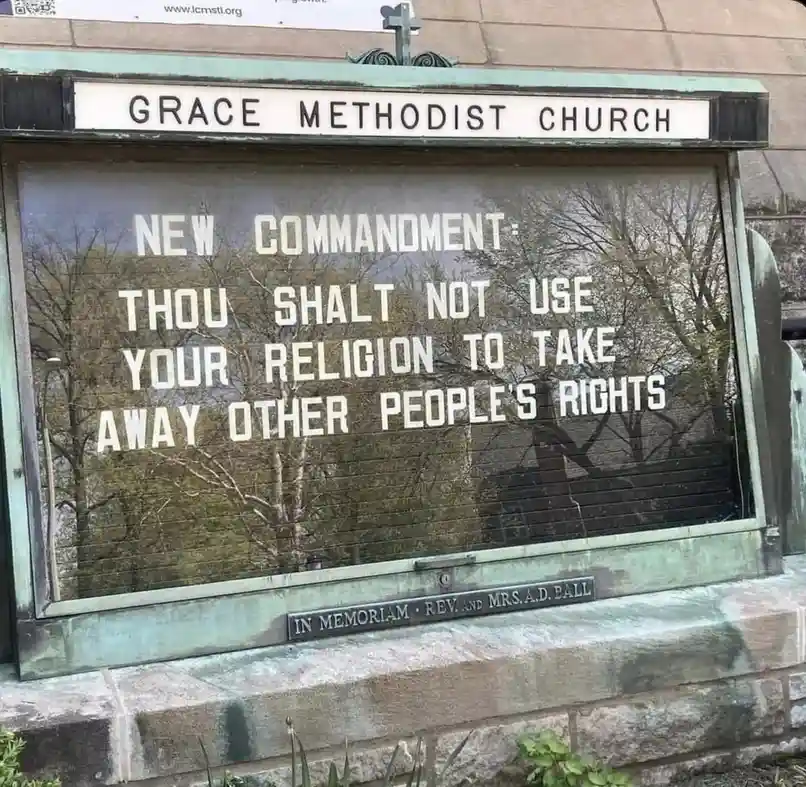 A weathered church sign for Grace Methodist Church displays a satirical 'new commandment' in white lettering: 'THOU SHALT…