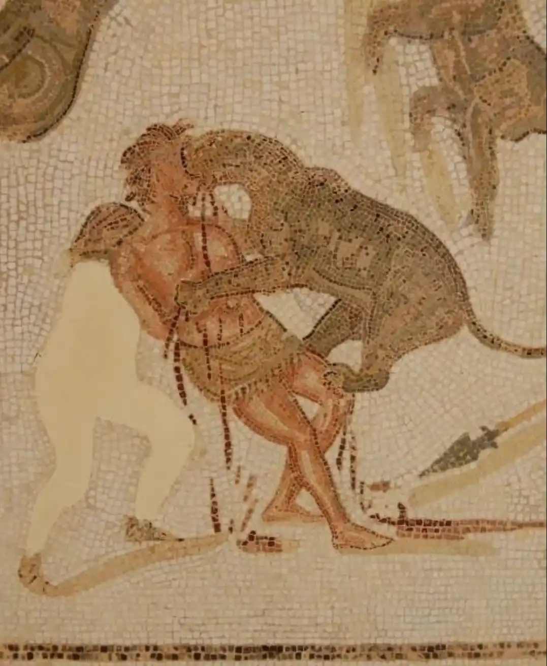 An ancient mosaic depicts a man being attacked by a large beast, with a second figure standing nearby. The overlaid text…