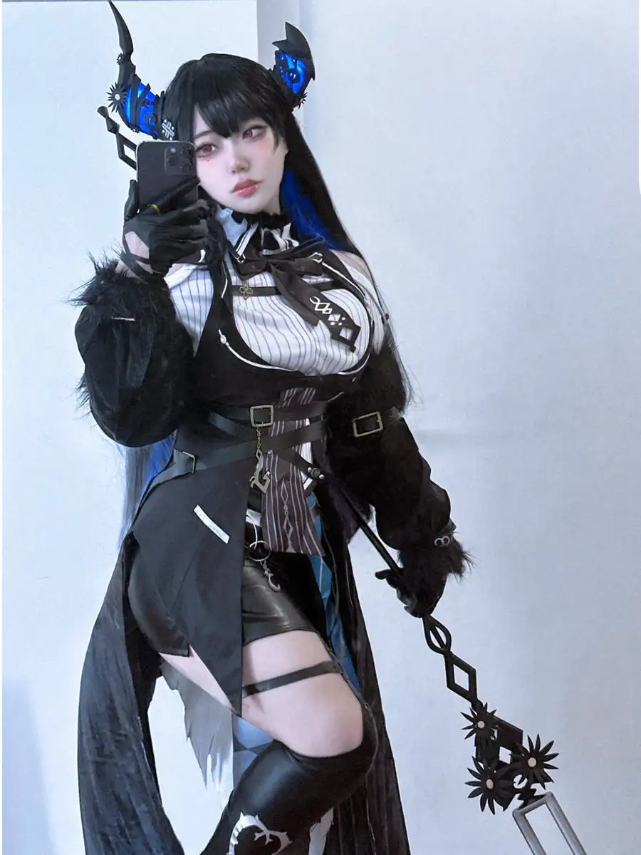 A person in a detailed devil-themed cosplay, featuring black horns with blue glowing accents, a black and white striped top…