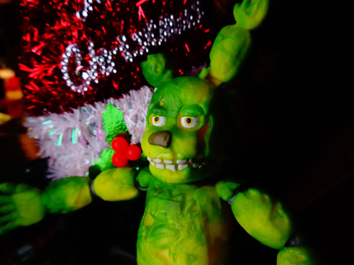 A green animatronic bear with a stitched mouth and wide eyes, resembling Freddy Fazbear from Five Nights at Freddy's, is…