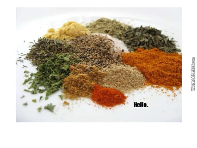 A white plate holds a colorful assortment of various dried herbs and ground spices, including green parsley, black pepper…