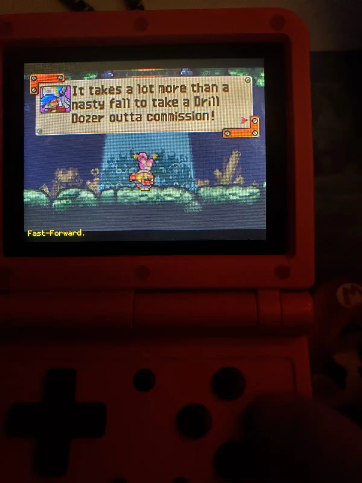 A red Nintendo 3DS displays a pixelated game scene from 'Kirby's Dream Land 3' where Kirby stands on a rocky platform. A…