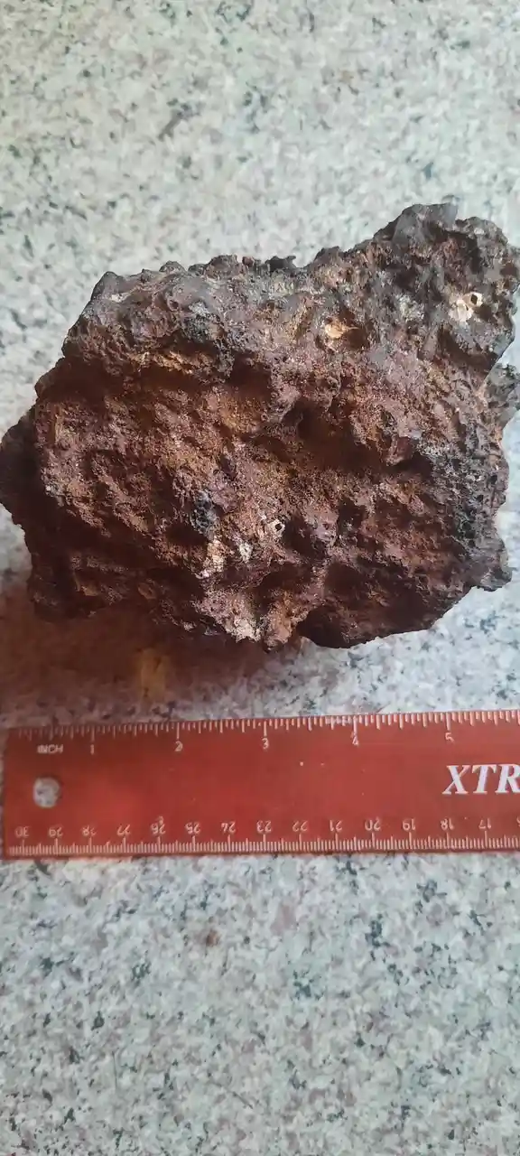 A rough, rusted, irregularly shaped metallic object, resembling a meteorite or corroded metal, rests on a speckled…