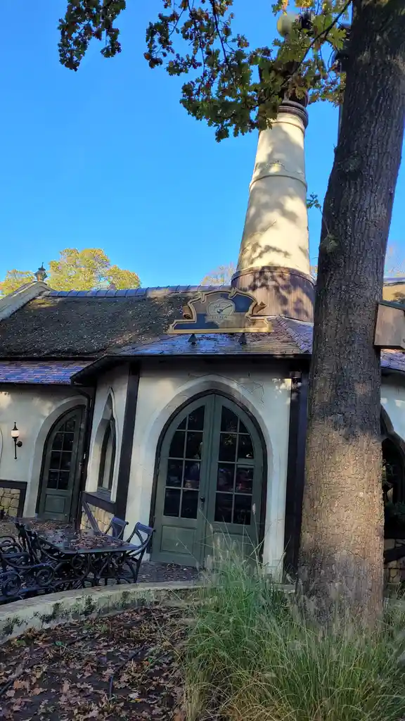 A quaint, rustic building with a thatched roof and arched green doors, featuring a large chimney and a sign reading 'polles…