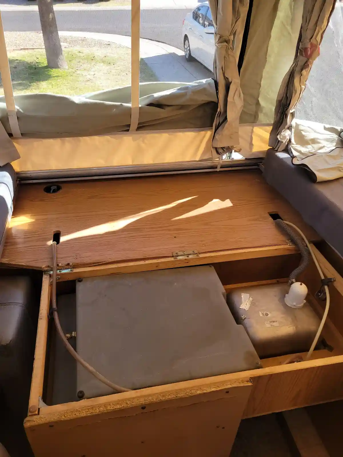 An open storage compartment in an RV reveals two gray propane tanks inside, with hoses connected. The compartment is made of…