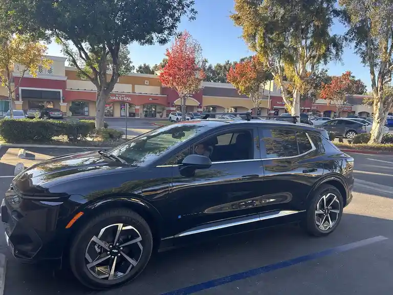 A black Chevrolet Equinox SUV is parked in a sunny shopping mall parking lot, with a person visible in the driver's seat…