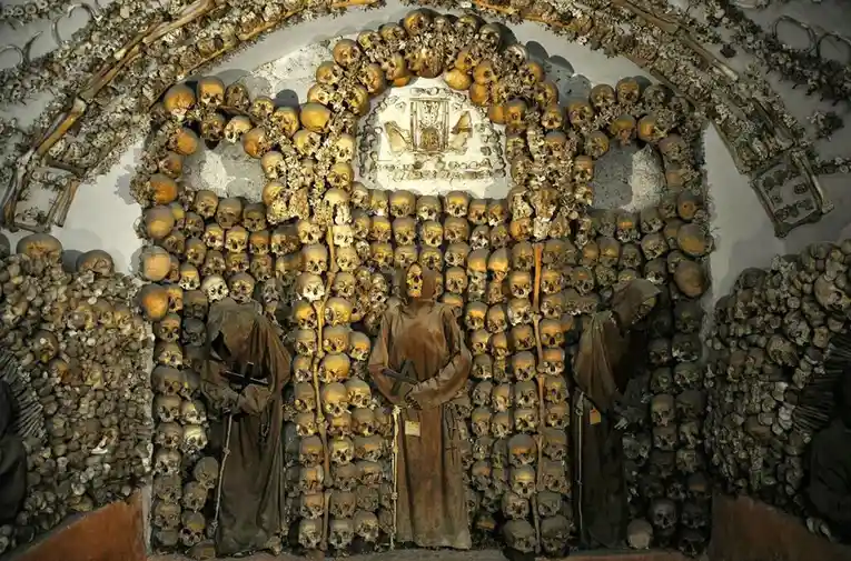 An image of a bone chapel, likely the Capuchin Crypt in Rome, where walls and arches are covered in human skulls and bones…